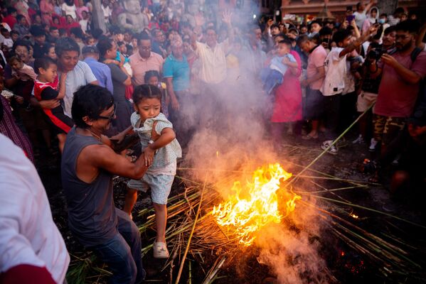 Un creyente sostiene a su niño sobre el fuego durante una festividad para celebrar la victoria sobre el malvado demonio Ghantakarna y la expulsión de los espíritus malignos, Nepal. - Sputnik Mundo