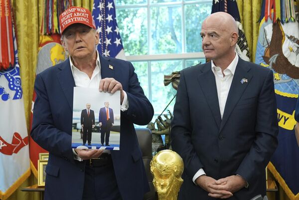 El presidente de EEUU, Donald Trump, sostiene una foto de él mismo con el dirigente ruso, Vladímir Putin, ante la mirada del presidente de la FIFA, Gianni Infantino, en el Despacho Oval de la Casa Blanca. - Sputnik Mundo
