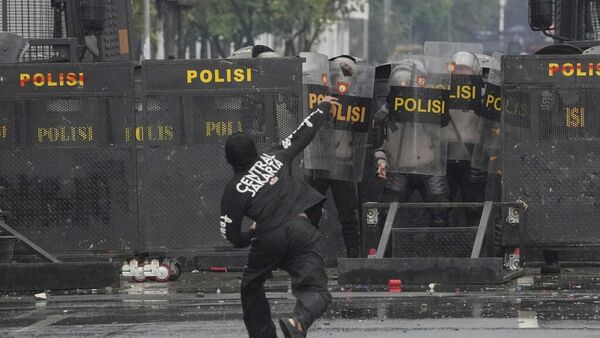 Agentes de Policía se cubren con escudos antidisturbios mientras un manifestante les arroja piedras durante una protesta contra las generosas asignaciones otorgadas a los miembros del Parlamento, frente al Parlamento en Yakarta, Indonesia, el 31 de agosto, 2025 - Sputnik Mundo