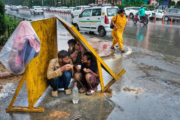 Los trabajadores beben té, sentados bajo paneles de sombra de hojalata para protegerse de la lluvia durante las obras viales, en Nueva Deli, India. - Sputnik Mundo