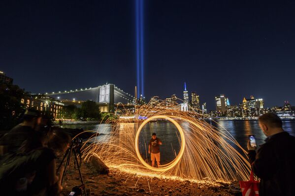 Una persona hace girar lana de acero frente a la instalación Homenaje en Luz, en recuerdo de los atentados del 11 de septiembre de 2001, que brilla en el cielo detrás del puente de Brooklyn, Nueva York.  - Sputnik Mundo