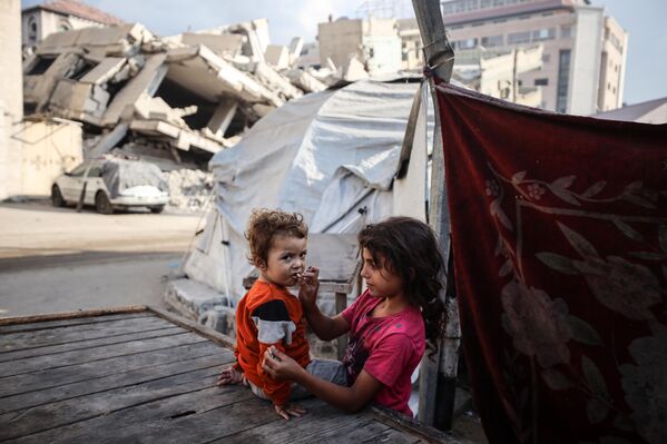 Una menor palestina desplazada alimenta a su hermana con pan frente a la escuela Farabi, que se ha convertido en un refugio tras ser alcanzada por un ataque israelí, en la ciudad de Gaza. - Sputnik Mundo