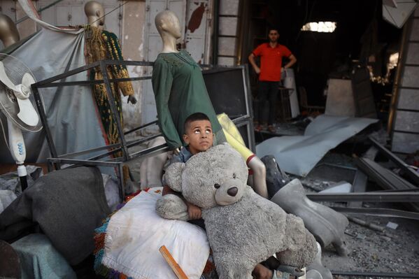 Niño palestino sostiene un juguete frente a los escombros de un edificio destruido por un ataque israelí. - Sputnik Mundo