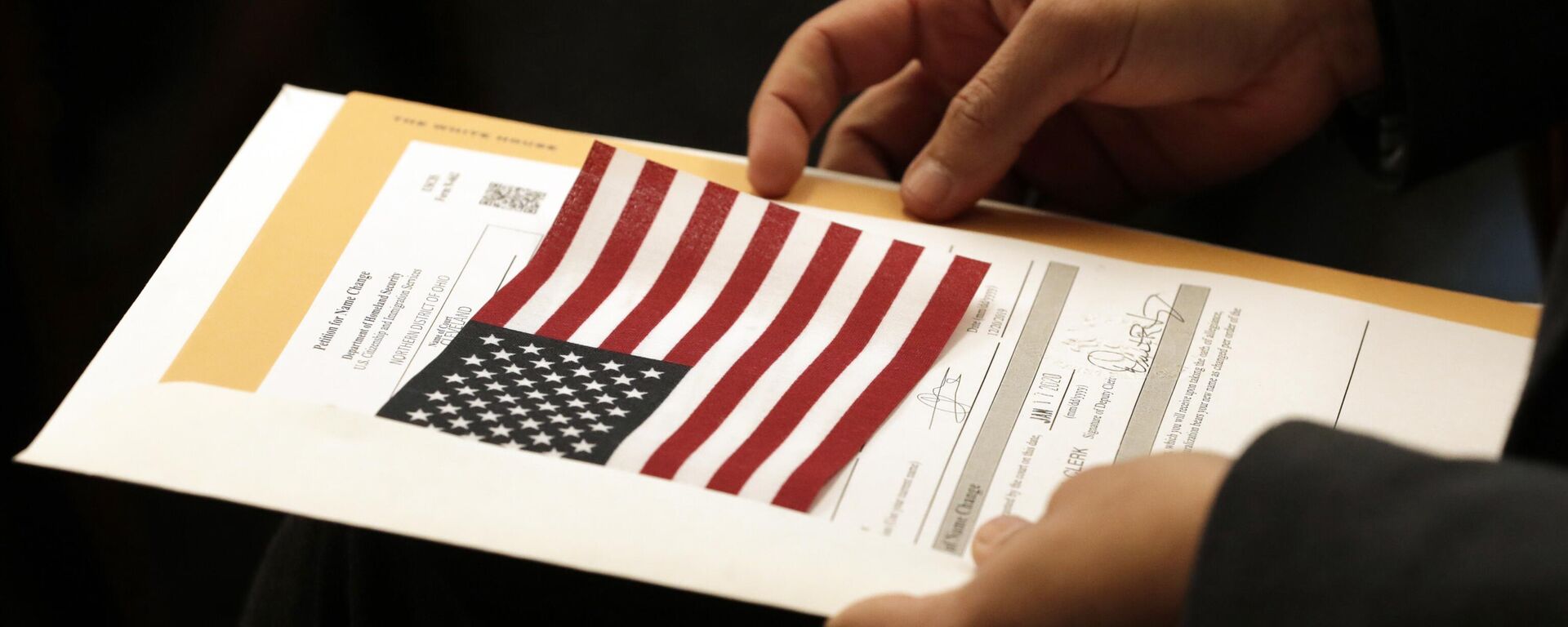 Paquete informativo y bandera estadounidense de un refugiado durante la ceremonia de naturalización - Sputnik Mundo, 1920, 04.10.2025