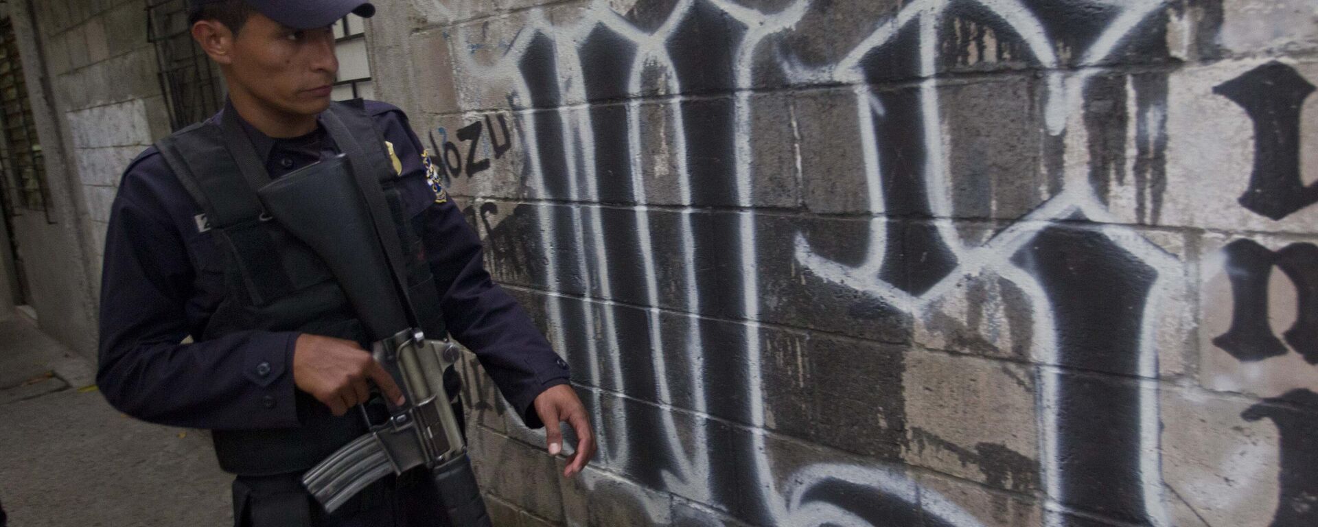 Un miembro de la Policía Nacional de El Salvador camina junto al símbolo de la pandilla Mara Salvatrucha pintado en una pared durante un operativo antipandillas en San Salvador, El Salvador (imagen referencial). Un miembro de la Policía Nacional de El Salvador camina junto al símbolo de la pandilla Mara Salvatrucha pintado en una pared durante un operativo antipandillas en San Salvador, El Salvador (imagen referencial). - Sputnik Mundo, 1920, 24.10.2025