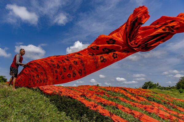 Un trabajador indonesio lanza una tela con estampado batik de colores a la orilla de un río en Sukoharjo, Java Central, Indonesia. La tela con estampado batik se procesa luego en una fábrica después de secarse y luego se vende a varias tiendas en Indonesia. - Sputnik Mundo