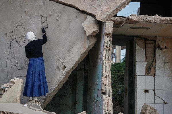 Una artista siria de grafiti dibuja un mural sobre el techo derrumbado de una casa dañada por la guerra en Daraya, a las afueras de Damasco, Siria. - Sputnik Mundo