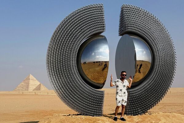 Un visitante de la exposición de arte contemporáneo en el histórico lugar de las pirámides de Guiza, Egipto, posa junto a una instalación. - Sputnik Mundo