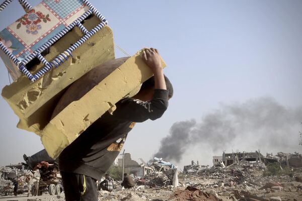 Palestinos llevan mantas y ropa recogidas en las ruinas de sus hogares, destruidos por los ataques israelíes en la Franja de Gaza. - Sputnik Mundo
