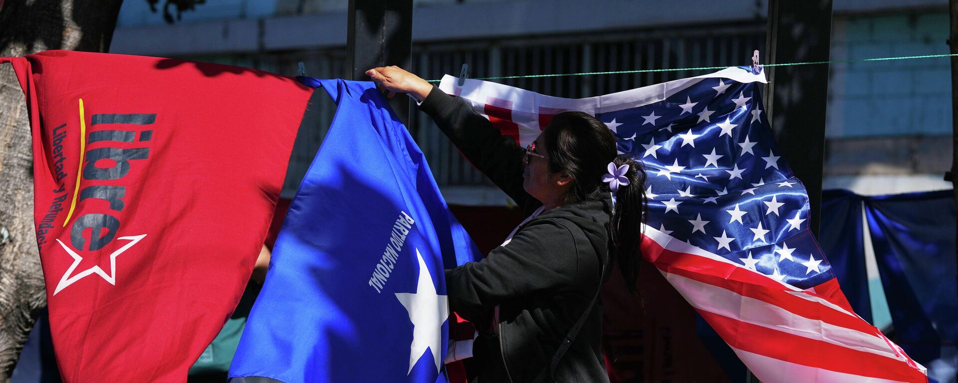 Vendedora ambulante cuelga banderas del partido Libre, Nacional y de los Estados Unidos - Sputnik Mundo, 1920, 29.11.2025