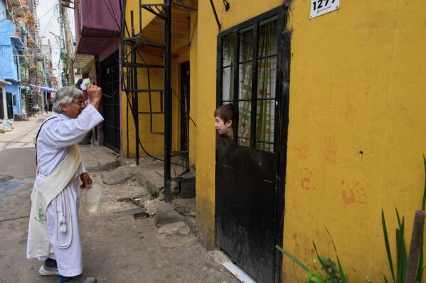 El diácono Mario René García bendice a Marcial Martínez, quien mira a través de la ventana de su casa durante una procesión que celebra la festividad de la patrona de Paraguay, Nuestra Señora de Caacupé, conocida popularmente como la Virgen Azul, en Buenos Aires, Argentina. - Sputnik Mundo
