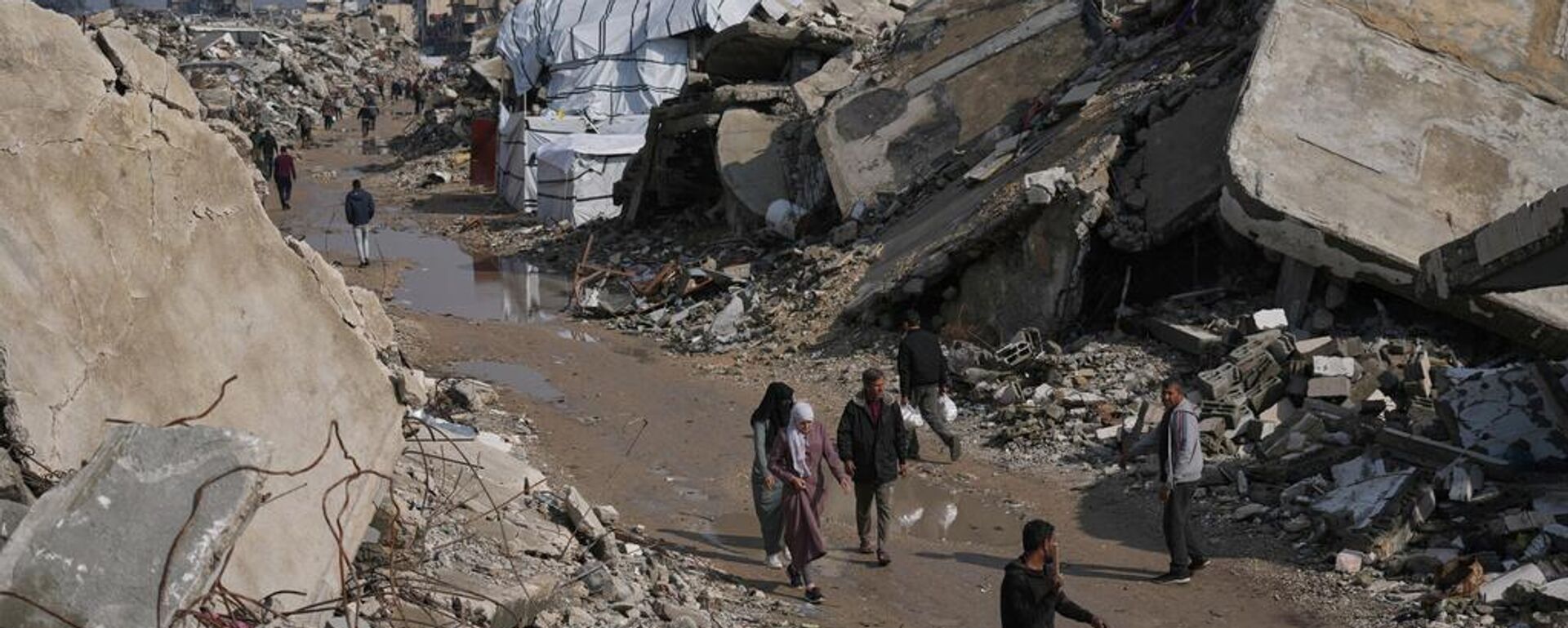 Palestinos caminan por una calle rodeada de edificios destruidos durante las operaciones aéreas y terrestres israelíes en la ciudad de Gaza, el miércoles 17 de diciembre de 2025. - Sputnik Mundo, 1920, 21.04.2026