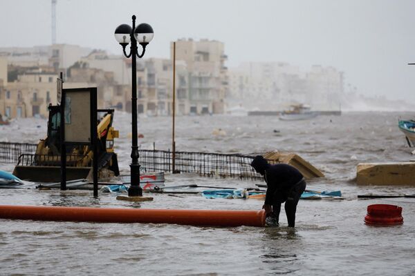 Un hombre arrastra un tubo desde una obra para utilizarlo a modo de dique durante una tormenta en Malta. - Sputnik Mundo