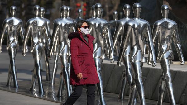 Una mujer pasa caminando junto a esculturas de personas exhibidas frente a un centro comercial en Pekín, China. - Sputnik Mundo
