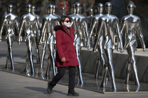 Una mujer camina delante de unas esculturas de personas expuestas frente a un centro comercial en la capital china, Pekín. - Sputnik Mundo