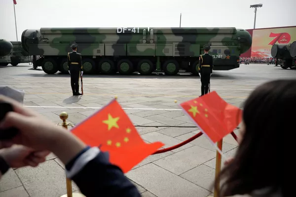 Los espectadores ondean banderas chinas mientras vehículos militares que transportan misiles balísticos nucleares DF-41 avanzan durante un desfile - Sputnik Mundo