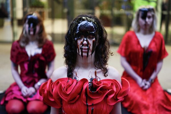 Activistas con vestidos de rosas rojas y rostros cubiertos de melaza se sientan afuera de las oficinas de Equinor —una compañía estatal noruega de petróleo— organizando una protesta por un derrame de petróleo, en Londres, Reino Unido.  - Sputnik Mundo
