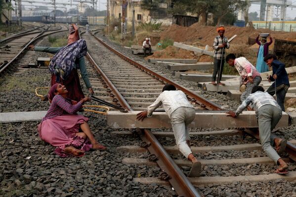 Una trabajadora reacciona al caer, mientras movía una traviesa de hormigón junto con otras personas en una vía férrea cerca de una estación de tren en Ahmedabad, India. - Sputnik Mundo
