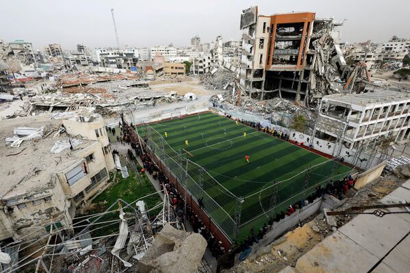 Palestinos juegan fútbol en un campo, cerca de edificios destruidos durante la ofensiva israelí de dos años, en la ciudad de Gaza. - Sputnik Mundo
