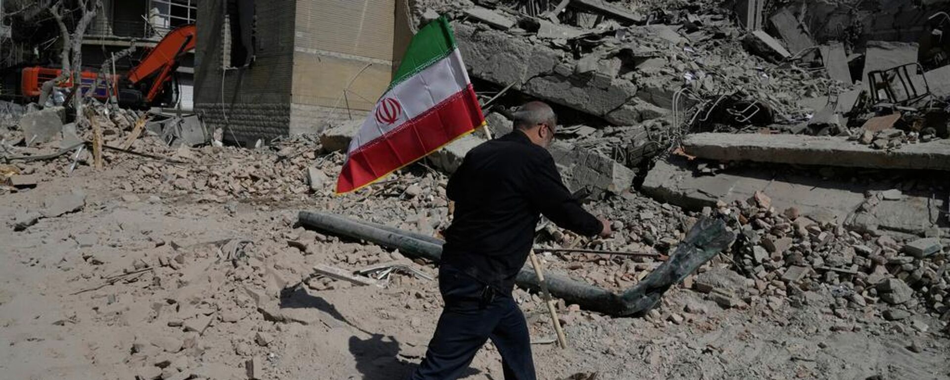 Un hombre lleva una bandera iraní para colocarla sobre los escombros de una instalación policial alcanzada durante la campaña militar estadounidense-israelí en Teherán - Sputnik Mundo, 1920, 30.03.2026