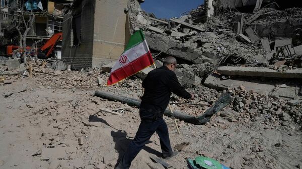 Un hombre lleva una bandera iraní para colocarla sobre los escombros de una instalación policial alcanzada durante la campaña militar estadounidense-israelí en Teherán - Sputnik Mundo