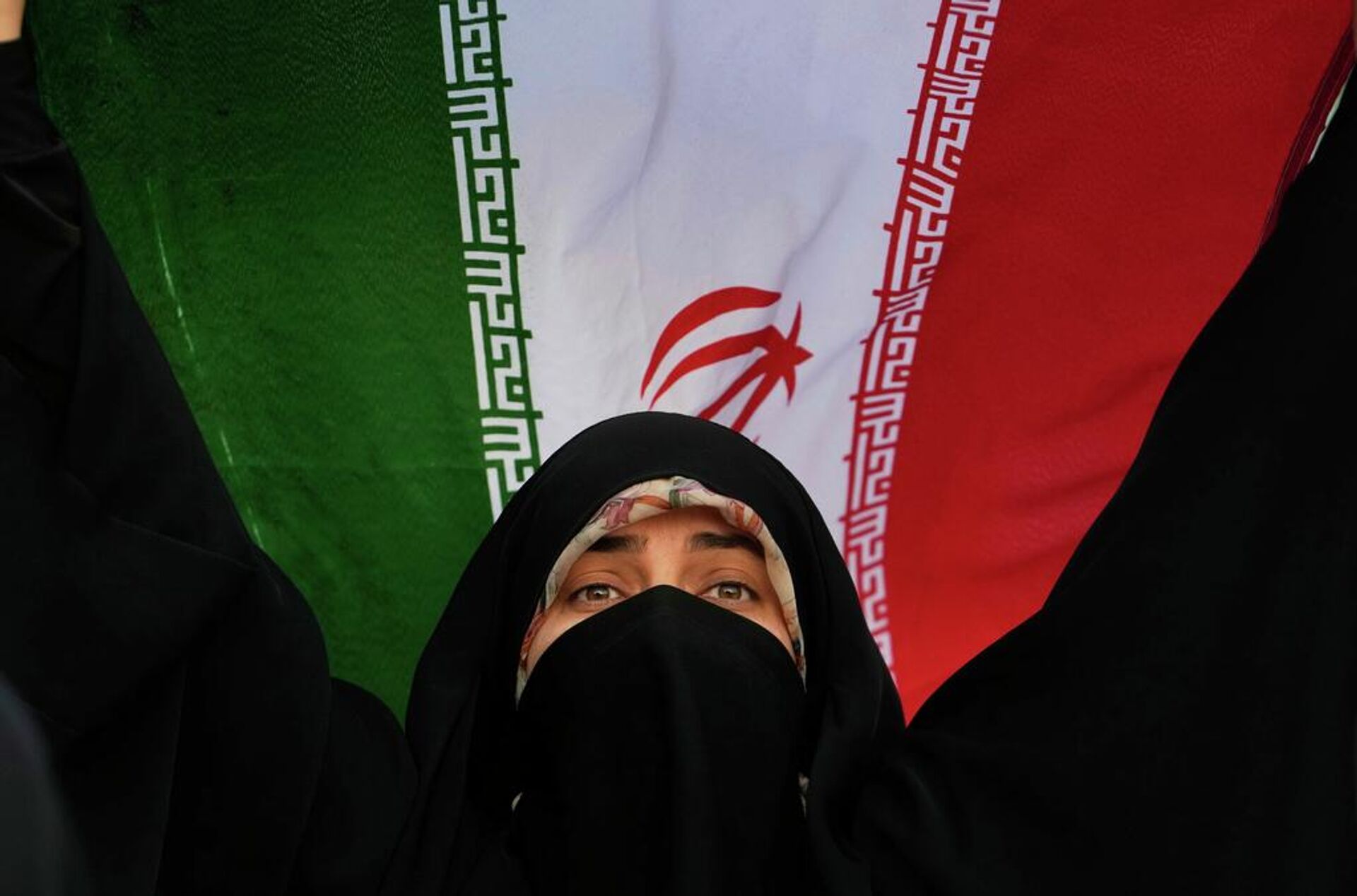 Una mujer iraní sostiene la bandera de su país en una manifestación contra EEUU e Israel en la plaza Enqelab-e-Eslami (Revolución Islámica), en el centro de Teherán, Irán, el 24 de junio de 2025.  - Sputnik Mundo, 1920, 07.03.2026