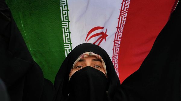 Una mujer iraní sostiene la bandera de su país en una manifestación contra EEUU e Israel en el centro de Teherán - Sputnik Mundo