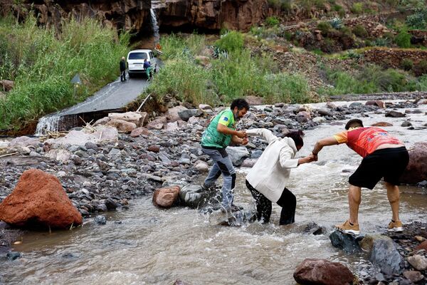 Dos hombres ayudan a una mujer a cruzar una zona inundada tras las fuertes lluvias provocadas por la tormenta Therese que azotó la isla de Gran Canaria. - Sputnik Mundo