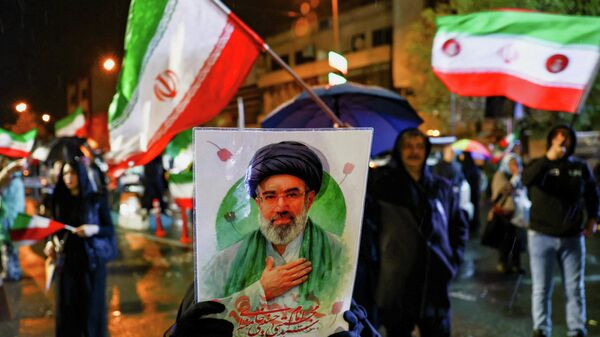 Una mujer sostiene un cartel que muestra al nuevo líder supremo de Irán, Mojtabá Jameneí, durante una manifestación antiestadounidense y antiisraelí, en medio del conflicto entre Estados Unidos e Israel con Irán, en Teherán, Irán, el 26 de marzo de 2026 - Sputnik Mundo