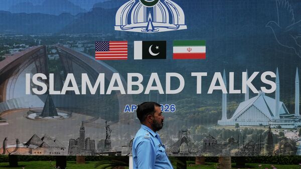 Un agente de Policía pasa junto a una valla publicitaria sobre las negociaciones entre Estados Unidos e Irán, frente a un centro de atención a los medios de comunicación en Islamabad, Pakistán, el 11 de abril de 2026 - Sputnik Mundo
