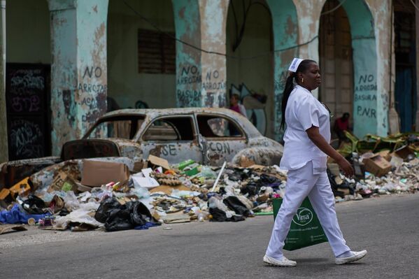 Una enfermera camina junto a la basura y un auto clásico abandonado en una calle de La Habana, Cuba. - Sputnik Mundo