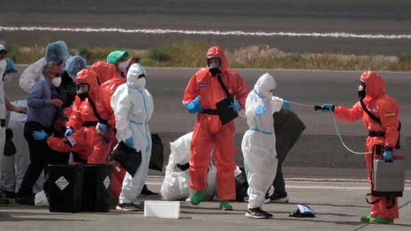 Los pasajeros son rociados con desinfectante por funcionarios del gobierno español antes de abordar un avión tras desembarcar del crucero MV Hondius, afectado por el hantavirus, en el aeropuerto de Tenerife, en las Islas Canarias, España, el domingo 10 de mayo de 2026. (Foto AP/Arturo Rodríguez) - Sputnik Mundo