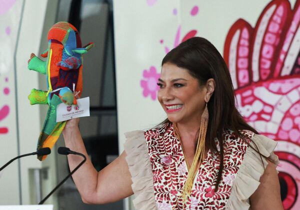 Sin embargo, el águila no es el único símbolo del Mundial de Fútbol 2026.  La mascota oficial de la capital mexicana es un ajolote con penacho que fue presentado por la jefa de Gobierno de la Ciudad de México, Clara Brugada. El ajolote representa la cultura mexicana y la transformación de la ciudad. En la foto: Clara Brugada sostiene un ajolote de juguete durante la inauguración de la línea de tren ligero renovada por el Gobierno de la ciudad, uno de los proyectos de infraestructura clave para mejorar la accesibilidad durante la Copa Mundial, en la Ciudad de México. - Sputnik Mundo