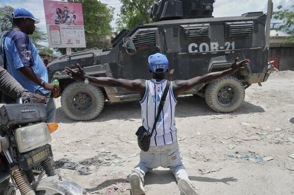 Un residente de la capital haitiana, Puerto Príncipe, se arrodilla ante un vehículo blindado policial y pide a la Policía que tome medidas contra las bandas que controlan su barrio. - Sputnik Mundo