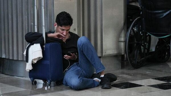Un pasajero observa su teléfono inteligente mientras espera en el Aeropuerto Internacional Benito Juárez de la Ciudad de México (archivo) - Sputnik Mundo