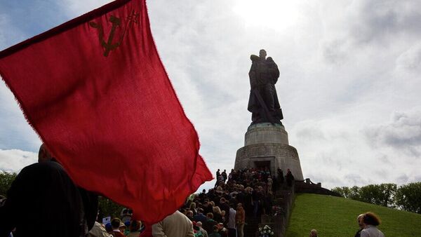 Un hombre sostiene una bandera soviética frente a una fila de personas durante una ceremonia de ofrenda floral para celebrar el Día de la Victoria en el Monumento Conmemorativo a los Soldados Soviéticos y el cementerio militar del Treptower Park, en Berlín, Alemania - Sputnik Mundo