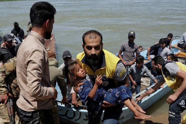 Un miembro de la Defensa Civil Siria, también conocidos como los Cascos Blancos, carga a un niño después de que los niveles de agua aumentaran debido al incremento de los desembalses tras las fuertes lluvias de este año, Deir ez-Zor, Siria. - Sputnik Mundo