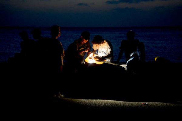 Un hombre repara una cuerda de guitarra a la luz de una linterna en el malecón de La Habana durante un apagón. - Sputnik Mundo