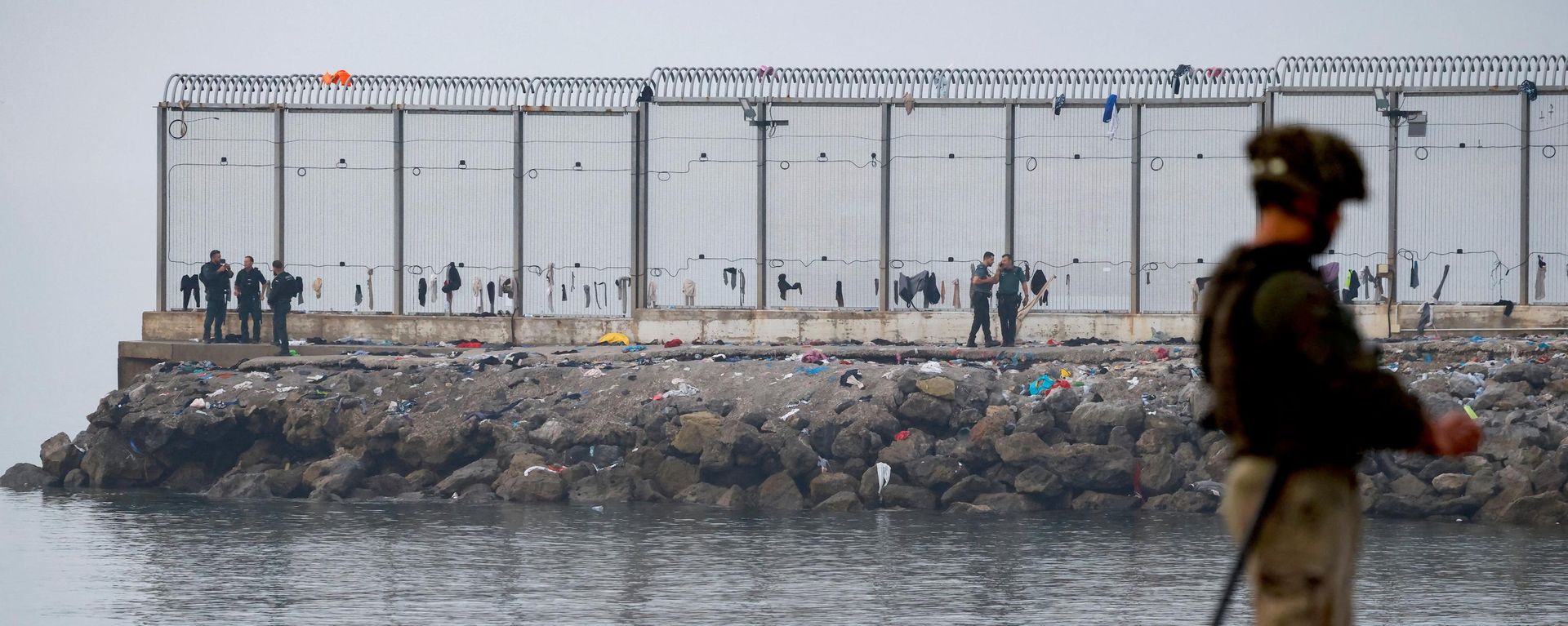 Agentes de seguridad españoles se encuentran cerca de la frontera, mientras un numeroso grupo de migrantes es escoltado hasta allí para ser expulsado de España tras los cruces masivos de migrantes a pie y por mar desde Marruecos hacia territorio español, en Ceuta, España, el 1 de agosto de 2026 - Sputnik Mundo, 1920, 01.08.2026