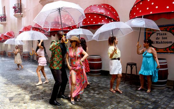 Personas bailan con paraguas en una 'calle lluviosa' con clima controlado en el complejo Voco Dubai Monaco, situado en el desarrollo The Heart of Europe, en Dubái, Emiratos Árabes Unidos (EAU). La atracción genera lluvia bajo demanda y mantiene la temperatura en torno a los 27 grados Celsius, mientras los promotores de EAU exploran formas de hacer más confortables los espacios al aire libre durante la temporada de verano en la región. - Sputnik Mundo