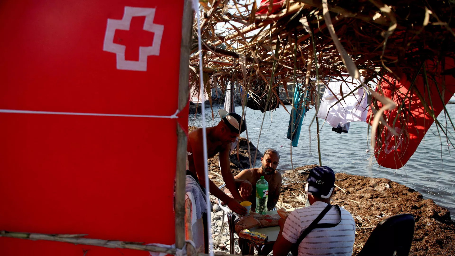 Migrantes marroquíes se sientan debajo de un refugio improvisado marcado con una cruz roja en Ceuta Migrantes marroquíes se sientan debajo de un refugio improvisado marcado con una cruz roja en Ceuta - Sputnik Mundo, 1920, 17.08.2026