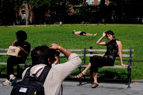 Una persona toma el sol mientras otras participan en una sesión de fotos durante una jornada de temperaturas cálidas en Washington Square Park, en Nueva York. - Sputnik Mundo