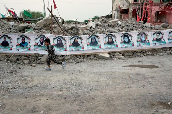 Un niño pasa corriendo junto a una pancarta colocada sobre las ruinas de la escuela iraní Shajare Tayebe en la ciudad de Minab, en la que hasta 180 alumnas y maestros murieron a causa de un bombardeo estadounidense. - Sputnik Mundo