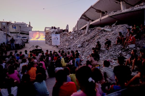 Niños palestinos desplazados en la ciudad de Gaza ven una película entre los edificios destruidos por los bombardeos israelíes. - Sputnik Mundo