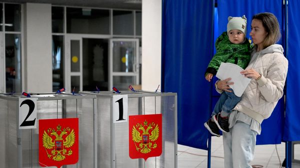 Una mujer con un niño en brazos vota en las elecciones a la Duma Estatal de Rusia de la novena legislatura - Sputnik Mundo