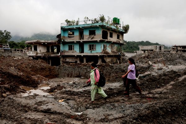 Personas pasan junto a viviendas dañadas tras unas mortales inundaciones repentinas y un deslizamiento de tierra, en Devighat, distrito de Nuwakot, Nepal. - Sputnik Mundo