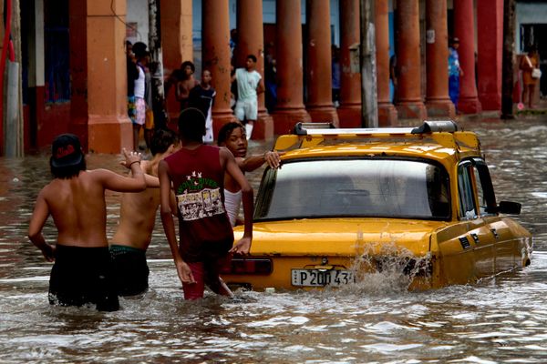Personas empujan un automóvil a través de las aguas de una inundación tras las fuertes lluvias en La Habana, Cuba. - Sputnik Mundo
