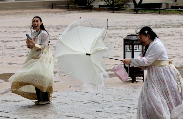 Turistas vestidos con hanbok, el traje tradicional coreano, reaccionan ante las fuertes ráfagas de viento mientras recorren el palacio de Gyeongbok, en Seúl. - Sputnik Mundo