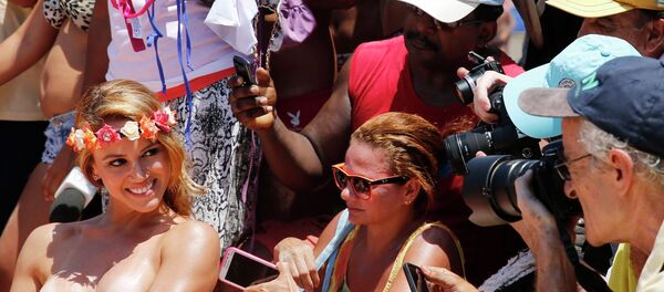 A woman poses with her top off as people take pictures during a protest called Make topless, not war at Ipanema beach in Rio de Janeiro January 20, 2015. - Sputnik Mundo