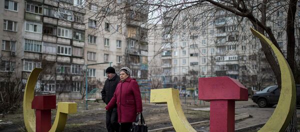 Local residents walk past Soviet-era hammer and sickle sculptures outside an apartment building damaged after Saturday's shellingin Mariupol, Ukraine - Sputnik Mundo